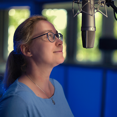 Katrin vor dem Mikrofon, um zu zeigen, wie deine Mitarbeitende praktische Übungen im Studio machen können Katrin vor dem Mikrofon, um zu zeigen, wie deine Mitarbeitende praktische Übungen im Studio machen können